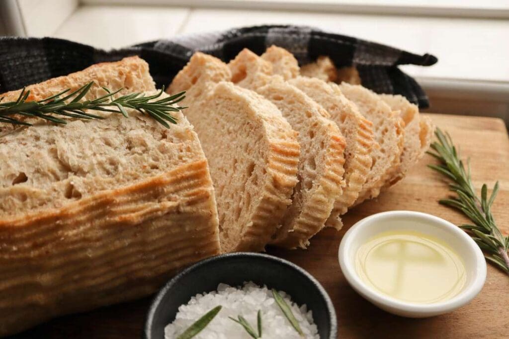 Freshly sliced sourdough bread on a wooden board, served with rosemary, olive oil, and sea salt, highlighting its artisan and healthy qualities.