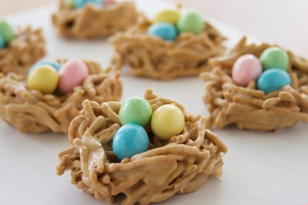 Homemade Easter bird’s nest treats made with peanut butter noodles and pastel-colored dye-free candy eggs on a white surface.